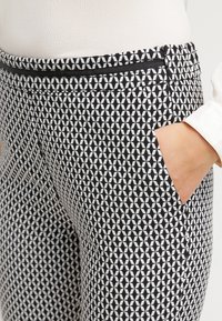 Zwart-witte broek met een geometrisch patroon, voorzien van zijzakken en een zwarte ritssluiting als accent op de tailleband.