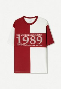 T-shirt a blocchi rossi e bianchi con scollatura rotonda. Presenta una stampa grafica con il testo "THE VICTORIOUS ARENA 1989" in un carattere bold.