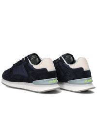 Marineblauwe suède sneakers met een grijze en witte zool. Voorzien van een lichtgekleurde hakaccent en een neonlogo aan de achterkant. Klassiek vetersluiting ontwerp.