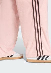 Pink fuzzy track pants with three brown side stripes, paired with white sneakers featuring black stripes and a gum sole.