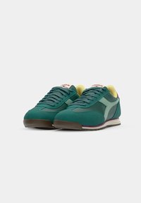 Groene sport schoenen van suede en mesh materialen, met een mintaccent, gele binnenkant en een bruine buitenzool met een paarse streep.