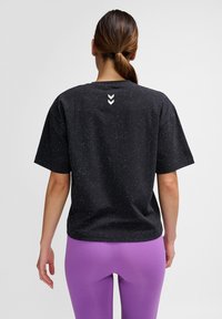 Svart prickig T-shirt med korta ärmar och avslappnad passform. Har en vit logotyp på baksidan och en mjuk bomullsliknande textur.