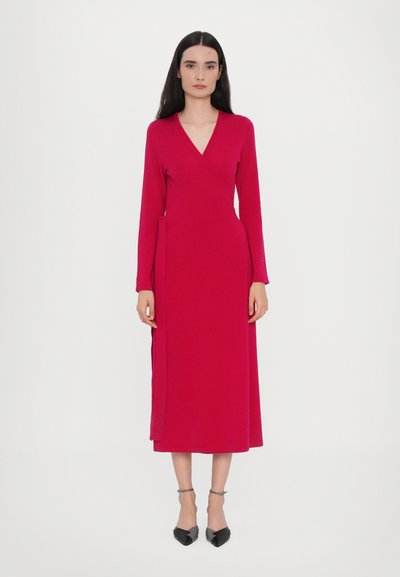 Rochie petrecută fucsia cu mâneci lungi și decolteu în V, prevăzută cu o curea laterală și o siluetă fluidă, asortată cu pantofi negri cu vârf ascuțit.