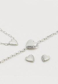 Σετ κοσμημάτων από ασήμι σε σχήμα καρδιάς που περιλαμβάνει μια αλυσίδα με κολιέ με κεντρική καρδιά διακοσμημένη με στρας και ταίριασμα σκουλαρίκια καρφωτά.