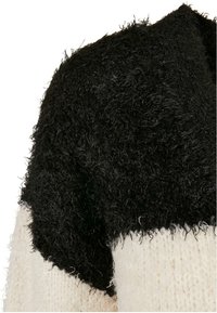 Svart fluffig stickad överdel övergår till en krämfärgad texturerad nederdel, vilket framhäver en distinkt färgblockering och varierande tygtexturer.