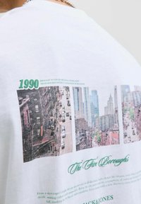 Baltos medvilnės marškinėliai su grafiniu miesto peizažų ir teksto spaudiniu. Savyje turi "1990" ir "Penki borough'ai" žalia spalvos šriftu.