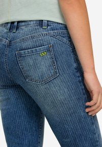 Slim jeans i blekt blå denim med vertikala ränder, som har en liten grön emblem på bakfickan och kontrastsöm.