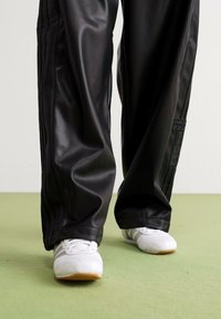 Baggy black faux leather trousers paired with white athletic shoes, featuring side stripes and a subtle sheen on the fabric.