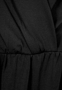 Tissu noir avec une texture froncée et plissée, présentant des plis diagonaux superposés créant un effet drapé.