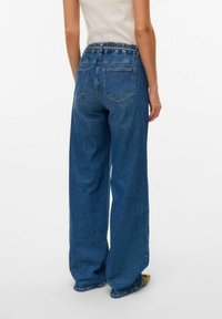 Szerokie niebieskie dżinsowe spodnie z elastycznym pasem, tylnymi kieszeniami i gładką fakturą, charakteryzujące się luźnym krojem i minimalnym przeszciem.