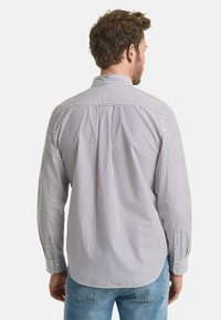 Chemise à rayures à manches longues en blanc, bleu et rouge. Présente un col classique, des poignets à boutons et un ourlet incurvé.