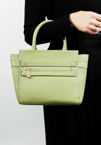 Groene leren handtas met een gestructureerd oppervlak, twee korte handvatten, een voorvak met rits en gouden hardware, en een rechthoekige vorm.