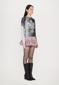 Long-sleeve graphic top with a dark design, paired with a pink frilled mini skirt and black knee-high heeled boots. Textured layers noted.