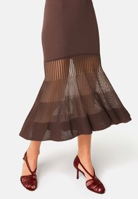 Bruine geribbelde gebreide rok met een sheer, gestreepte zoom. Gecombineerd met donkerrode strappy hoge hakken met een puntige neus.