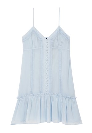 Donna che indossa un vestito azzurro chiaro senza maniche con bottoni e orlo arricciato, che tiene una borsa nera con catena argentata e scarpe nere con borchie.