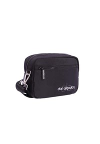 Bolso rectangular negro hecho de tela suave, con cierre superior, herrajes plateados y un logo en blanco en la parte frontal. Incluye una correa ajustable.