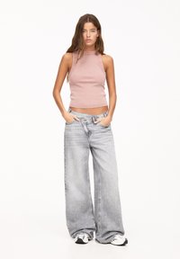 Top in cotone a costine rosa chiaro abbinato a jeans grigi chiari a vita alta e morbidi. L'outfit presenta un design corto e un collo alto.