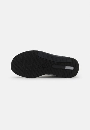 Semelle de chaussure en caoutchouc noir avec un motif de bande de roulement en zigzag et une petite section rectangulaire translucide près du talon sur fond blanc.