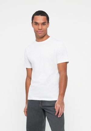 T-shirt en coton blanc avec un col rond et des manches courtes, associé à un jean gris foncé. Design simple et minimal sans motifs ni accents.