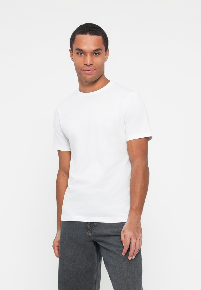 Witte katoenen t-shirt met ronde hals en korte mouwen, gecombineerd met donkergrijze jeans. Eenvoudig, minimalistisch ontwerp zonder patronen of accenten.