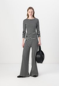 Haut à rayures noir et blanc à manches longues et pantalon évasé assorti en tissu doux ; le mannequin tient un sac à main rond noir.