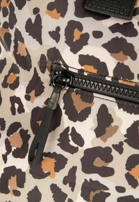 Tkanina s leopardím vzorem v béžové, hnědé a černé barvě s uzávěrem na zip, který má černý kovový zip a nastavitelný jezdec.