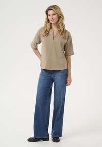 Top beige de manga corta con escote en V y un corte holgado, combinado con jeans azul de pierna ancha. Los jeans tienen una textura clásica de denim.