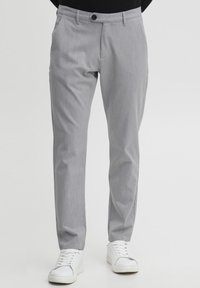 Pantalones grises claros a medida con frente plano, textura vertical sutil y bolsillos estándar, combinados con zapatillas blancas.