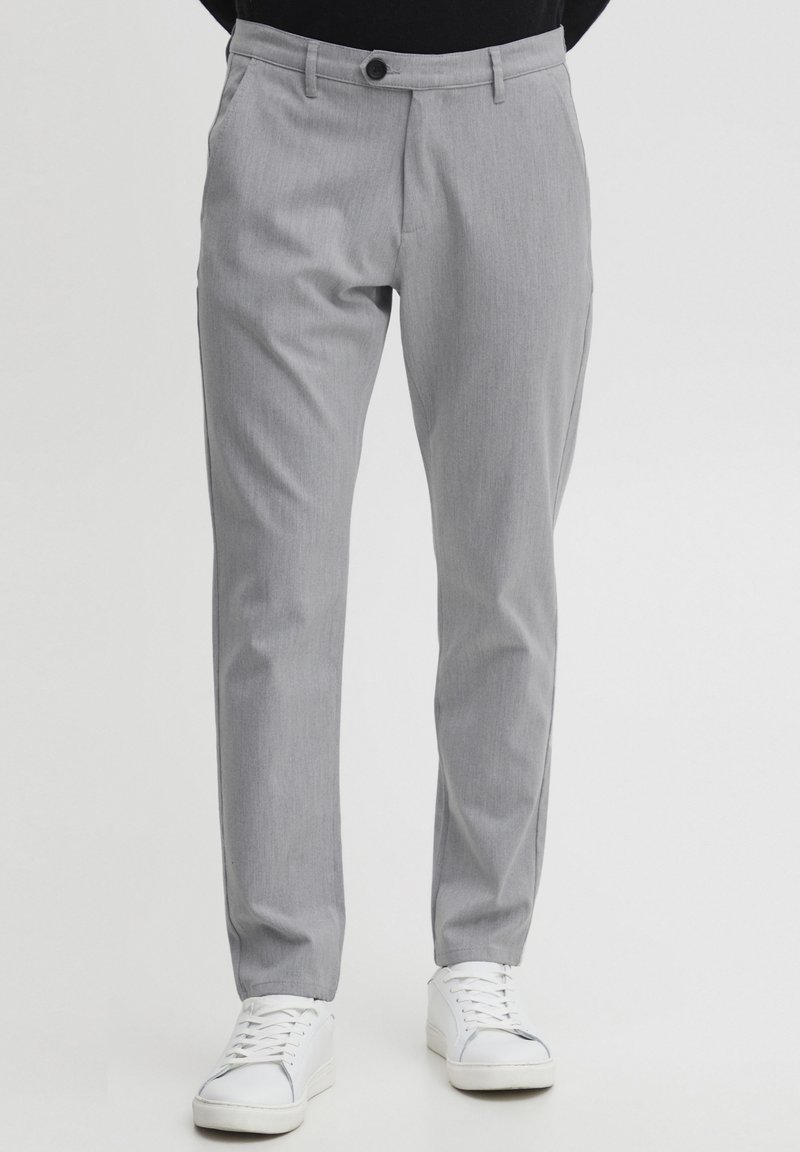 Pantalones grises claros a medida con frente plano, textura vertical sutil y bolsillos estándar, combinados con zapatillas blancas.