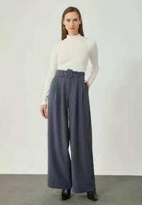 Kõrge vöökohaga tume sinine laia jala pükste komplekt, millel on voldid ja millel on vööl vöö, koos sobiva valge pika varrukaga pluusiga.