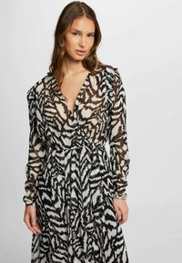 Abito lungo e trasparente con una stampa astratta a righe bianche e nere che richiama il motivo di una zebra, scollatura a V, maniche a volant e vita adatta.