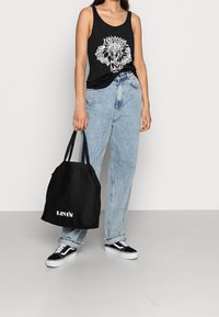 Svart linne med vit elefantgrafik, ljusblå högmidjade jeans, svart canvasryggsäck med vit "Levi's"-logotyp och svarta sneakers.