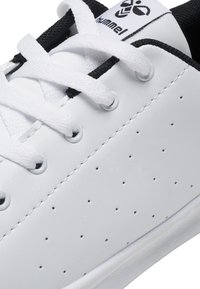 Hvit lær sneakers med perforerte detaljer, svarte aksenter og hvite lisser. Har runde hull og en flat gummi såle.