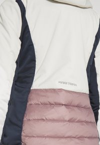 Pufferjakke med hvit overdel, marineblå sideseksjoner og mauve nedre del. Materialet er glatt med sydd horisontal detaljering.