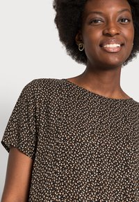 Blusa preta de manga curta com padrão floral em branco, bege e azul claro. Tecido suave com um corte relaxado e decote redondo.