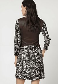 Vestido de estampado en blanco y negro con un corpiño de cuero marrón y largas mangas estampadas, presentando una tela texturizada y un detalle de cintura ceñida.