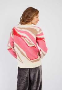 Pull en tricot avec un motif multicolore en rose, beige et rouge, doté d'un ourlet côtelé de couleur crème. Texture douce et coupe décontractée.