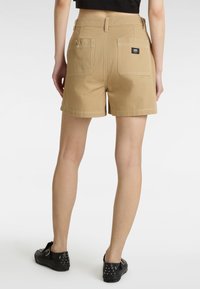 Pantalones cortos de mezclilla beige con un corte clásico, bolsillos laterales y traseros, y detalles de costura blanca. Combinados con zapatillas negras con tachuelas.