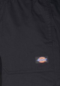 Černé pracovní kalhoty s texturovanou látkou, s boční kapsou a šitým logem na pravé straně.