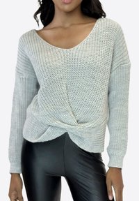 Lichtgrijze gebreide trui met een losse pasvorm, V-hals en gedraaide detail bij de taille. Gecombineerd met nauwsluitende zwarte legging. Gestructureerde stof.