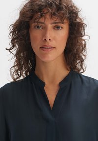 Dunkelblaues Hemd mit subtiler Schattierung, kurzem Stehkragen und Vorderpatte. Leichter Stoff mit glatter Textur und einfachem Design.