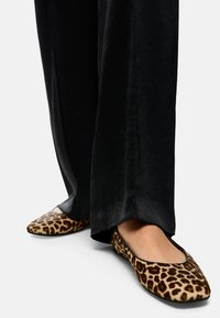 Leopard print flat shoes with a rounded toe design, made of soft fabric, paired with loose black pants.
