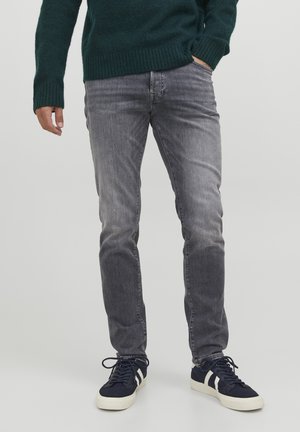 Gray denim jeans with a slim fit, featuring a faded finish. Paired with navy sneakers and a green knitted sweater.