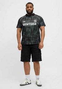 Jersey de patrón negro y gris con mangas cortas, que presenta un cuello y la palabra “VENTURA” en blanco. Combinado con pantalones cortos cargo negros y zapatillas.