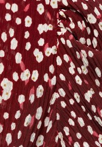 Tissu rouge avec une surface texturée présentant un motif de petites fleurs blanches et des accents roses, créant un design visuellement texturé.