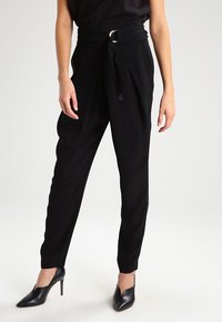 Svarta högmidjade byxor med bälte i knytning, som har en avslappnad passform och avsmalnande ben, parat med svarta klackskor.