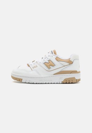 Witte en beige New Balance 550 sneaker met geperforeerd leer, "N"-logo en rubberen zool op een effen lichte achtergrond.