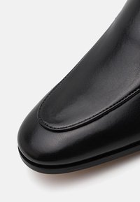 Black leather shoe with a smooth finish, rounded toe, and subtle stitching details. The sole is flat and slightly raised at the heel.