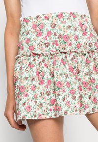 Blommig kjol med en smockad midja, med vit bakgrund, rosa och persikofärgade blommor samt en lager på lager volangnedre del. Texturerad tyg.