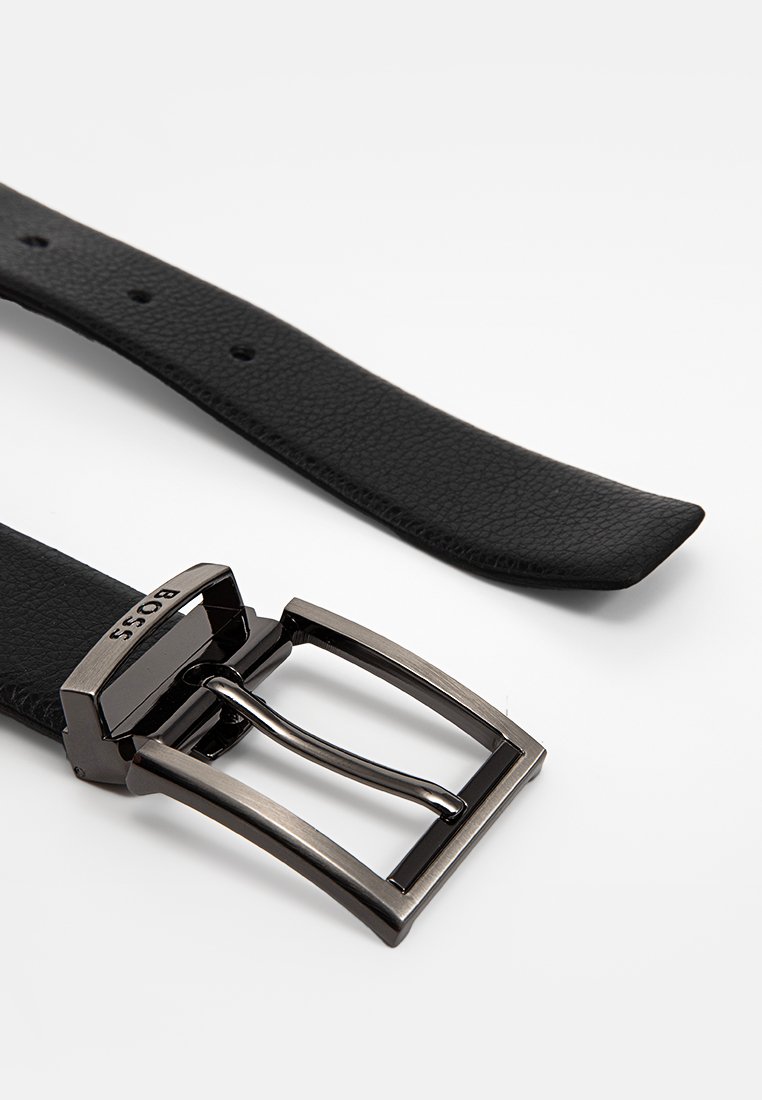Cintura in pelle nera con texture, dotata di una fibbia rettangolare metallica incisa con il nome del marchio "BOSS" su sfondo bianco.